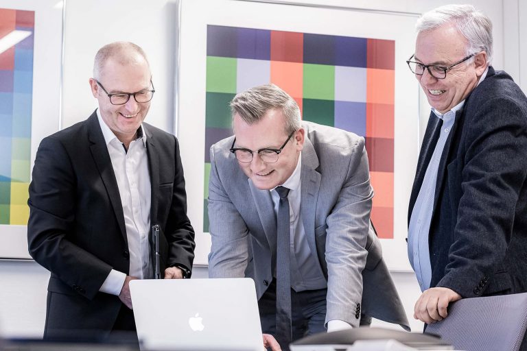 Drei Männer schauen auf einen Laptop.