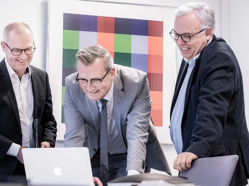 Drei Männer schauen auf einen Laptop.